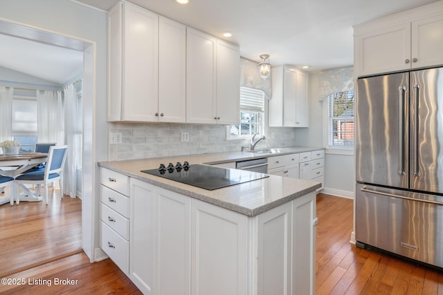 kitchen featuring light wood finished floors, tasteful backsplash, white cabinets, stainless steel appliances, and a sink