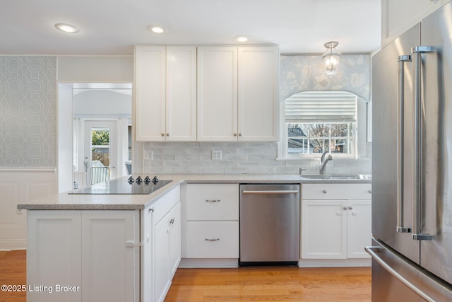 kitchen featuring a wainscoted wall, appliances with stainless steel finishes, white cabinetry, a sink, and wallpapered walls