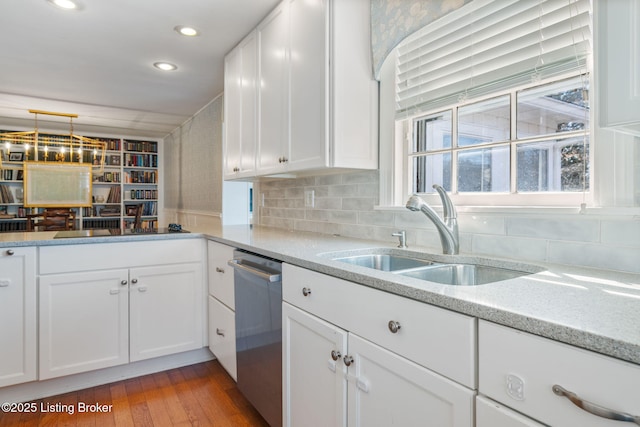 kitchen featuring tasteful backsplash, light wood-style flooring, stainless steel dishwasher, white cabinets, and a sink