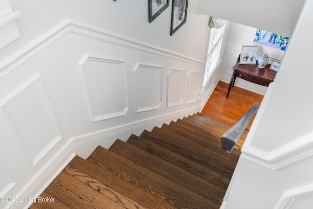 stairway with wainscoting, wood finished floors, and a decorative wall