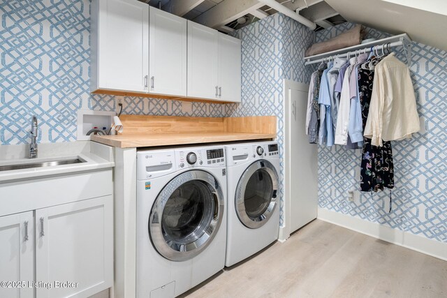 washroom with cabinet space, washing machine and dryer, a sink, light wood-type flooring, and wallpapered walls