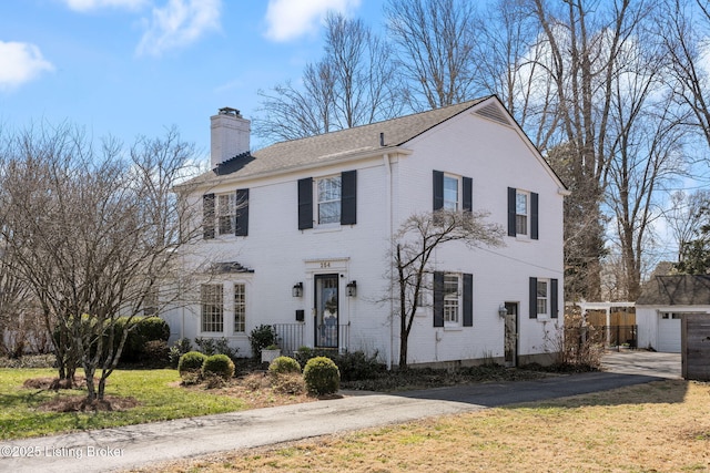 view of front of property with brick siding, a chimney, an outdoor structure, and a front yard