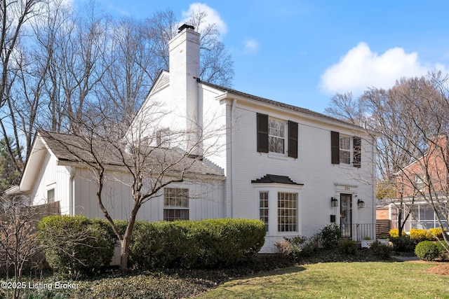 view of front of property featuring a front lawn, a chimney, and brick siding