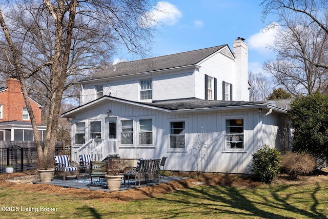 back of house featuring a chimney, roof with shingles, fence, a yard, and a patio area