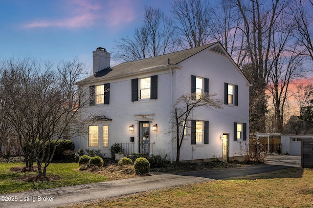 view of front facade with aphalt driveway, brick siding, a chimney, an outdoor structure, and a front lawn