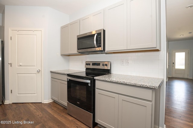 kitchen with light stone counters, gray cabinetry, stainless steel appliances, decorative backsplash, and dark wood-style floors