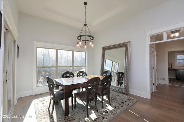 dining room featuring visible vents, baseboards, a tray ceiling, and wood finished floors