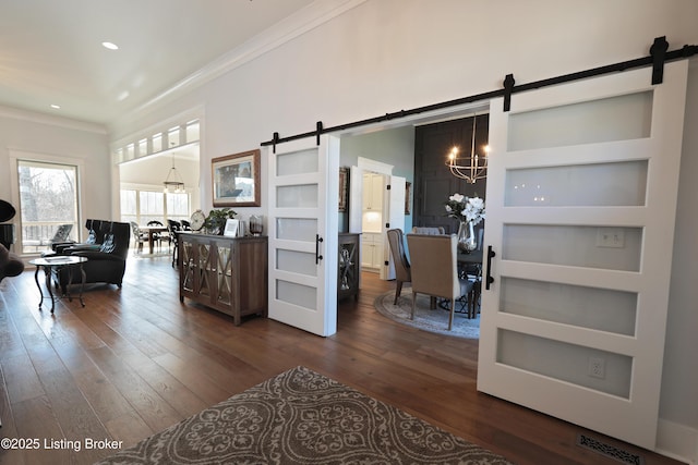 living area featuring dark wood-type flooring, crown molding, a barn door, recessed lighting, and a notable chandelier