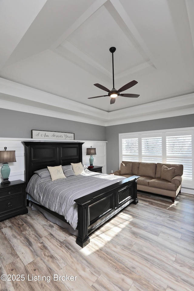 bedroom featuring light wood-type flooring, a raised ceiling, and a ceiling fan