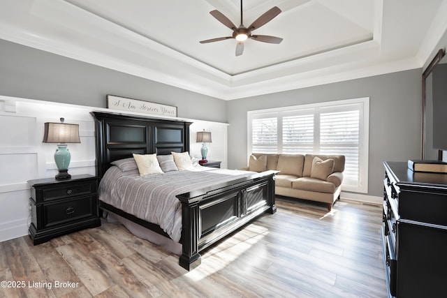 bedroom with a ceiling fan, a raised ceiling, and wood finished floors