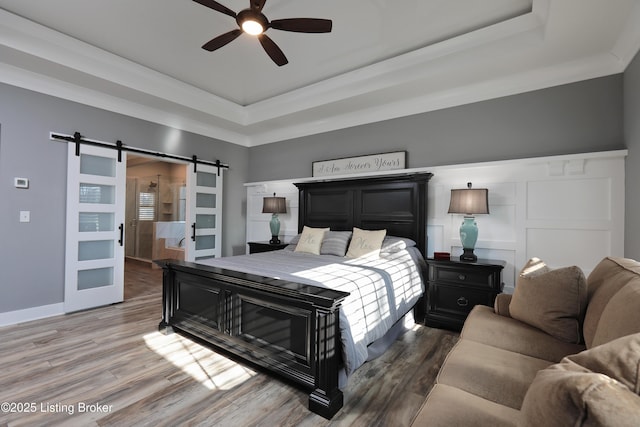 bedroom with a decorative wall, a raised ceiling, a barn door, and wood finished floors