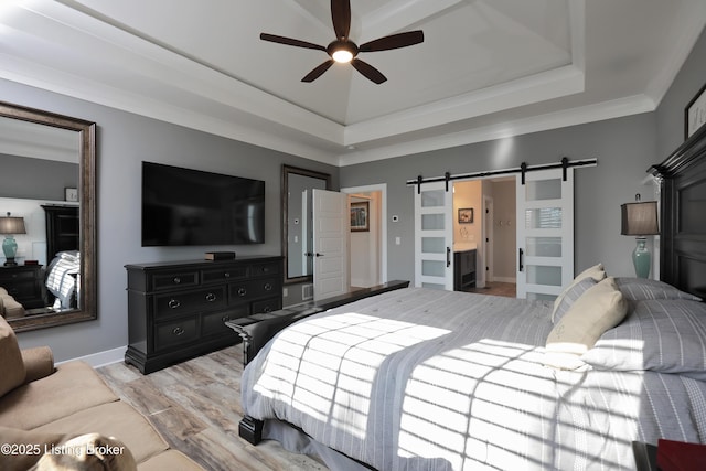 bedroom with baseboards, light wood-type flooring, a tray ceiling, a barn door, and ornamental molding