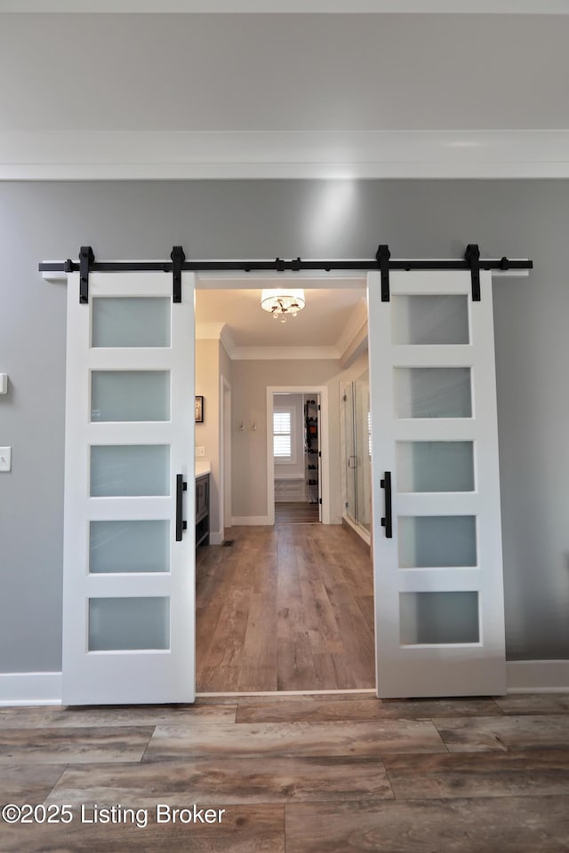 interior space featuring a barn door, wood finished floors, baseboards, and ornamental molding