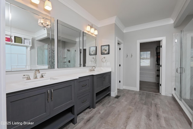 full bath with a sink, wood finished floors, ornamental molding, and a shower stall