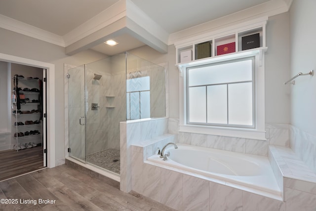 full bath featuring a spacious closet, a shower stall, crown molding, a garden tub, and wood finished floors