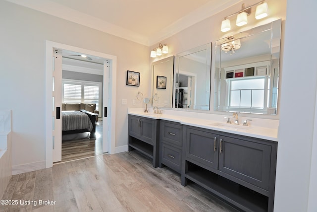 ensuite bathroom with ensuite bath, double vanity, wood finished floors, and a sink