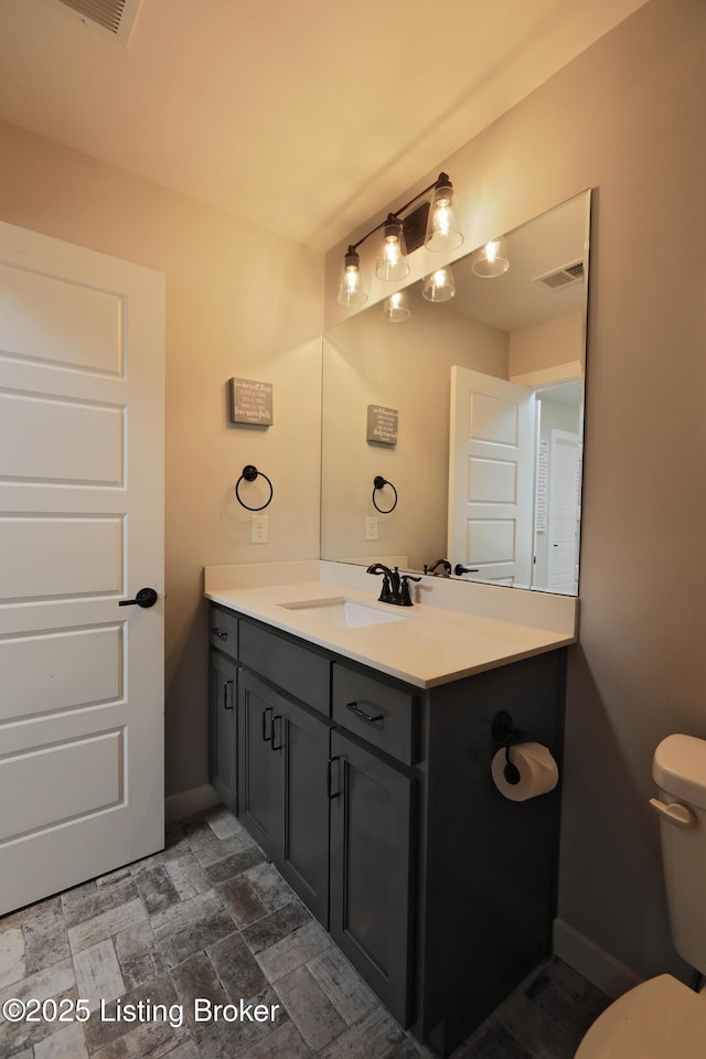 half bath featuring vanity, baseboards, visible vents, stone finish flooring, and toilet