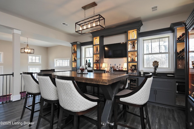 bar featuring indoor wet bar, dark wood-type flooring, visible vents, and pendant lighting