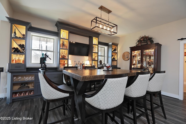 bar featuring dark wood finished floors, hanging light fixtures, baseboards, and indoor bar