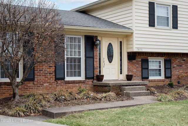 view of exterior entry featuring a shingled roof and brick siding