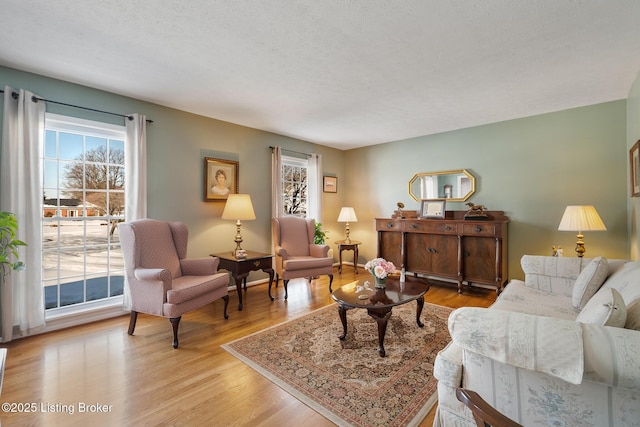 living area featuring a textured ceiling, light wood finished floors, and baseboards