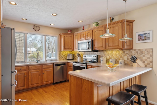 kitchen featuring backsplash, light wood-style flooring, appliances with stainless steel finishes, a sink, and a peninsula