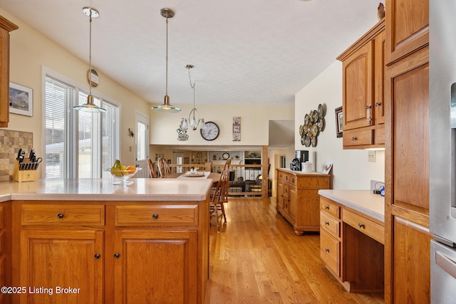 kitchen with light wood-style floors, light countertops, hanging light fixtures, and a peninsula