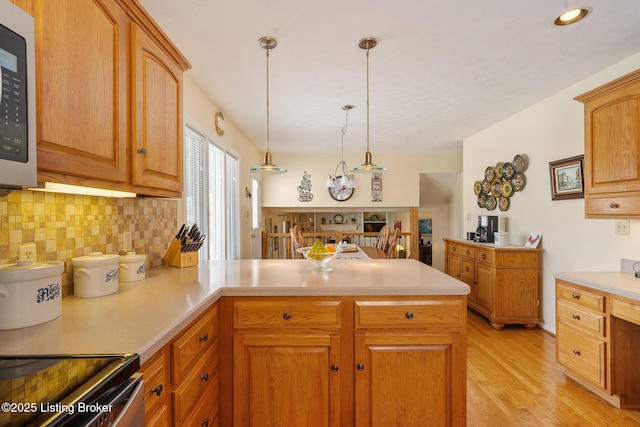 kitchen with light wood-style flooring, a peninsula, light countertops, tasteful backsplash, and decorative light fixtures