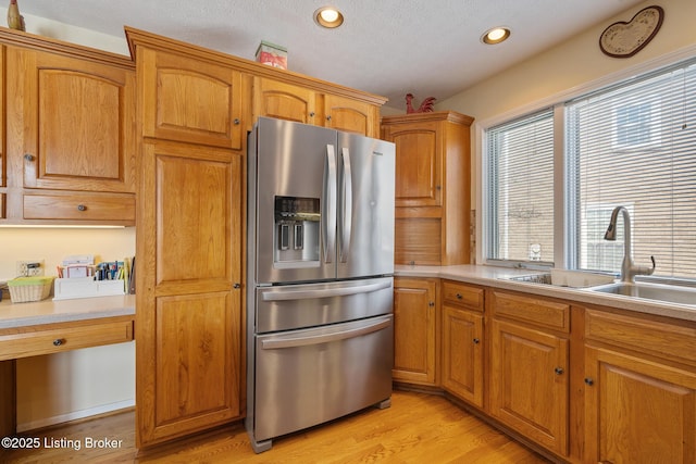 kitchen featuring a sink, light countertops, stainless steel refrigerator with ice dispenser, light wood finished floors, and brown cabinetry