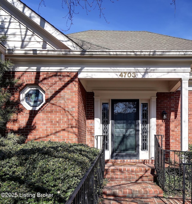 doorway to property featuring brick siding and roof with shingles