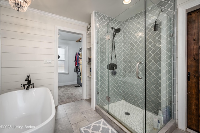 full bath with tile patterned floors, a walk in closet, a stall shower, ornamental molding, and a soaking tub