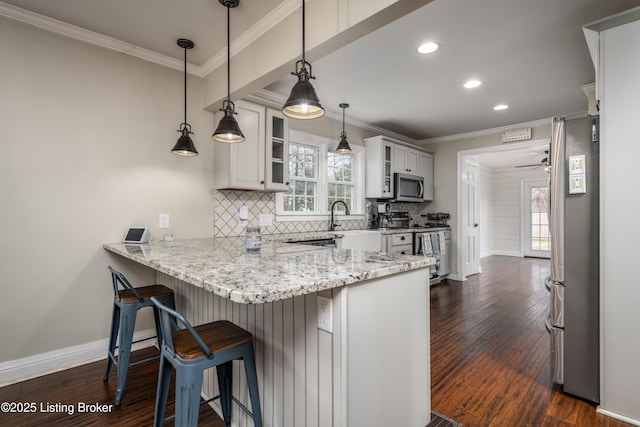 kitchen featuring a breakfast bar, tasteful backsplash, stainless steel appliances, a peninsula, and crown molding