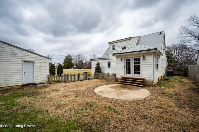 rear view of house with entry steps, french doors, metal roof, a fenced backyard, and a yard