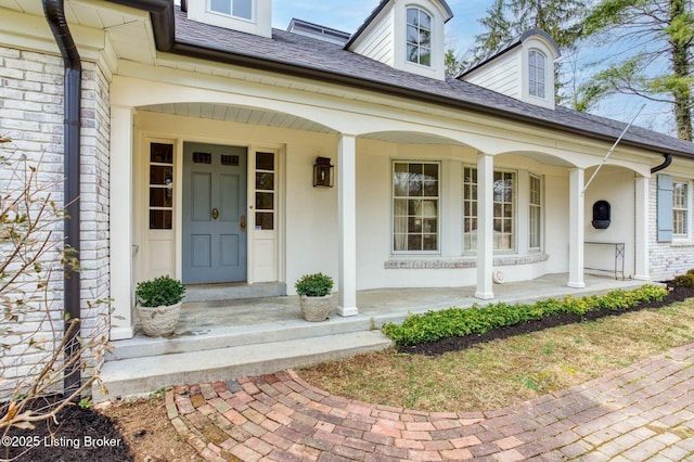 doorway to property with covered porch and a shingled roof