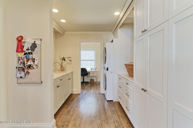 interior space with light wood-type flooring, ornamental molding, a sink, recessed lighting, and stacked washer / drying machine