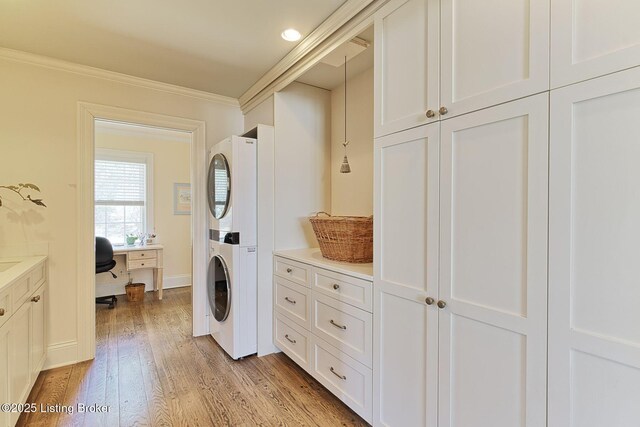 laundry room featuring light wood finished floors, stacked washing maching and dryer, crown molding, and baseboards