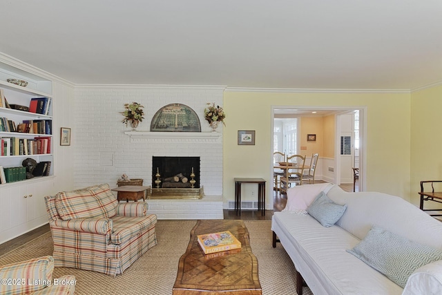 living room with built in shelves, wood finished floors, visible vents, ornamental molding, and a brick fireplace