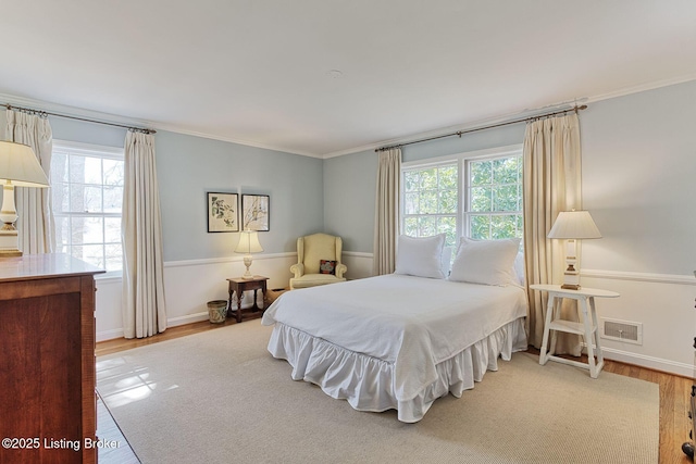 bedroom featuring light wood-style flooring, baseboards, visible vents, and ornamental molding