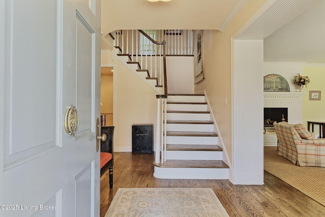 foyer entrance with baseboards, stairway, ornamental molding, a fireplace, and wood finished floors