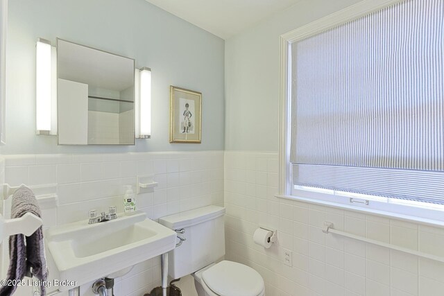 bathroom featuring a sink, a wainscoted wall, toilet, and tile walls