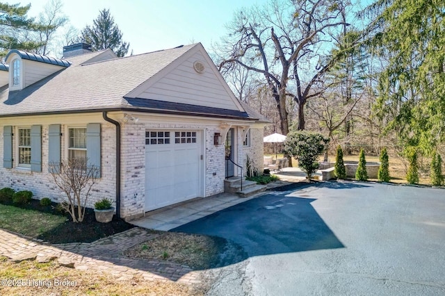 exterior space featuring brick siding, a shingled roof, aphalt driveway, a chimney, and an attached garage