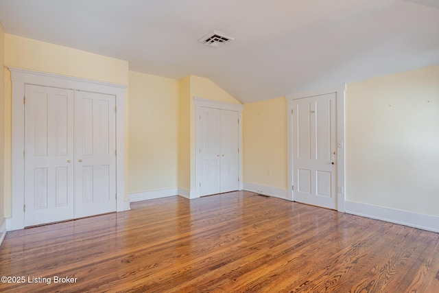 interior space featuring baseboards, visible vents, lofted ceiling, wood finished floors, and two closets