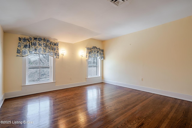 spare room with baseboards, visible vents, and wood finished floors