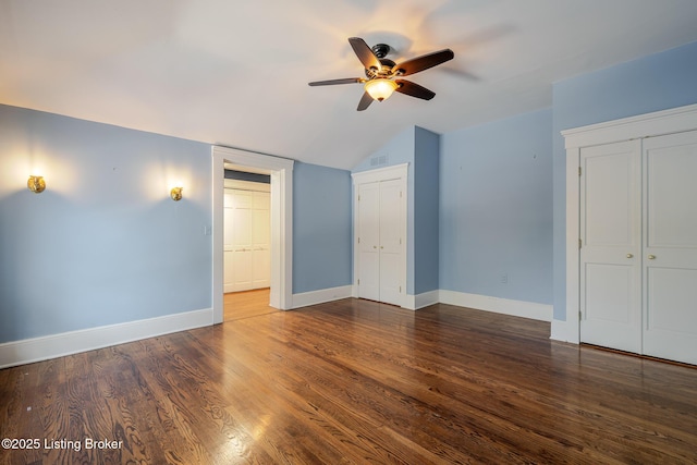 unfurnished bedroom featuring baseboards, lofted ceiling, ceiling fan, wood finished floors, and two closets