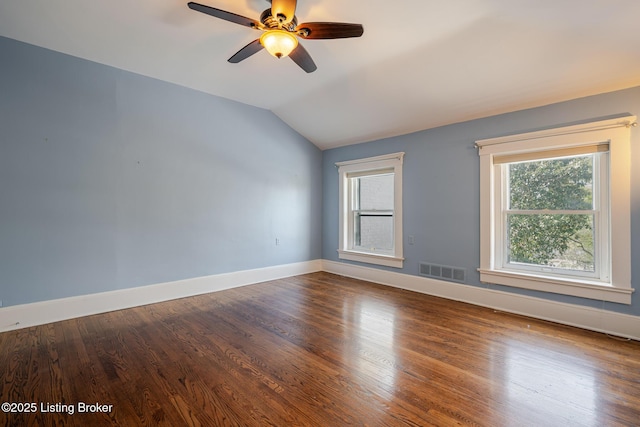 empty room with a ceiling fan, visible vents, vaulted ceiling, baseboards, and dark wood-style floors