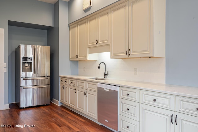 kitchen featuring stainless steel appliances, dark wood-type flooring, a sink, decorative backsplash, and light stone countertops