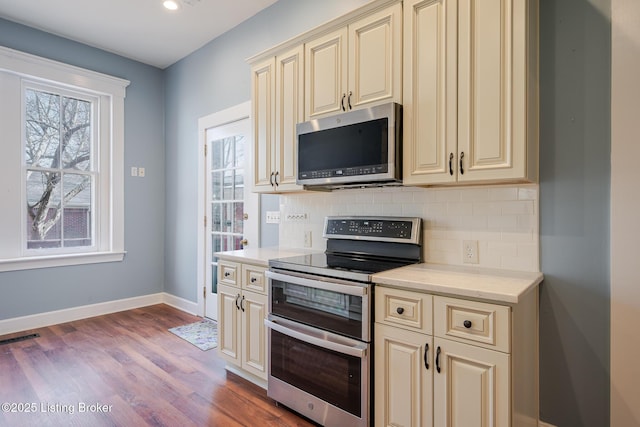 kitchen with baseboards, tasteful backsplash, appliances with stainless steel finishes, and cream cabinetry