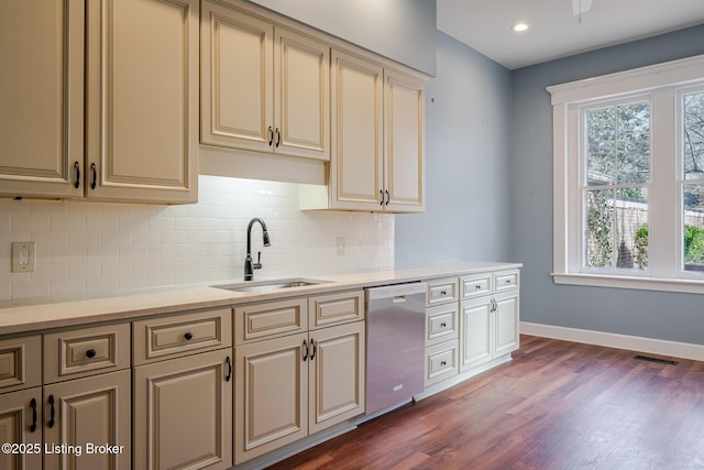 kitchen featuring dark wood-style floors, cream cabinetry, stainless steel dishwasher, a sink, and baseboards