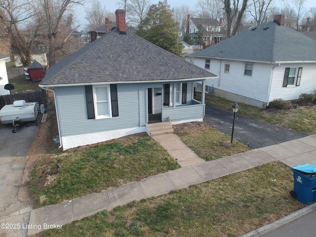 bungalow with a shingled roof, a chimney, a front lawn, and aphalt driveway