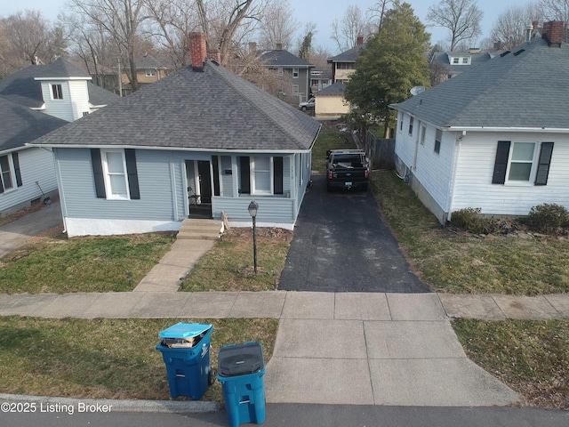 view of front of home featuring aphalt driveway, roof with shingles, and a chimney